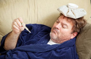 A man laying on a couch reading a thermometer