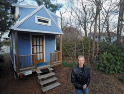 A tiny blue home with man standing outside in front of it