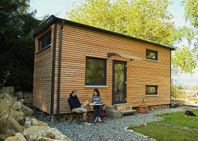 A tiny home with a man and women sitting along the front walkway